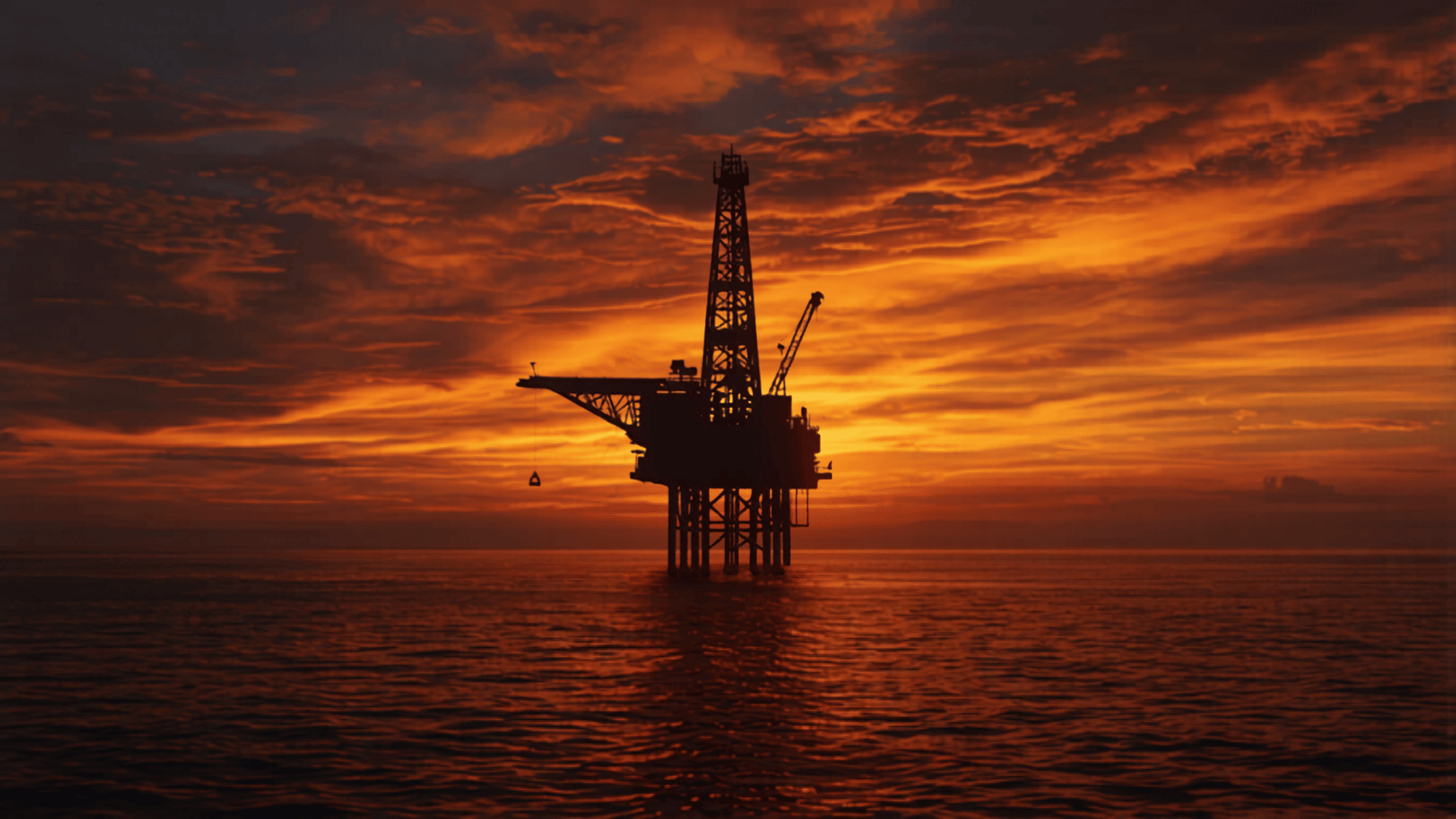 Offshore oil and gas platform silhouetted against a dramatic sunset sky.